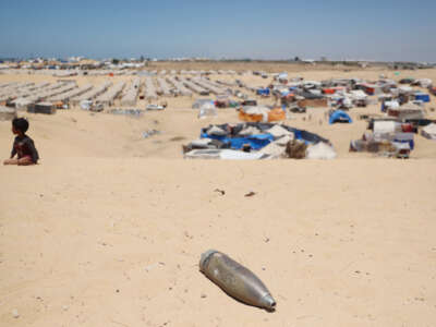 A child plays on a sand dune next to an unexploded ordnance, in view of the tent city in Rafah