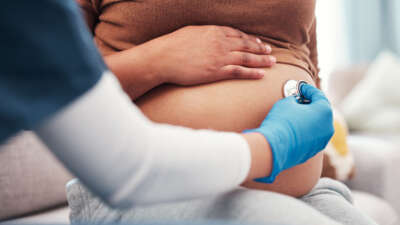 A health care worker performs a check-up with a stethoscope on a pregnant woman