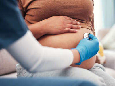 A health care worker performs a check-up with a stethoscope on a pregnant woman