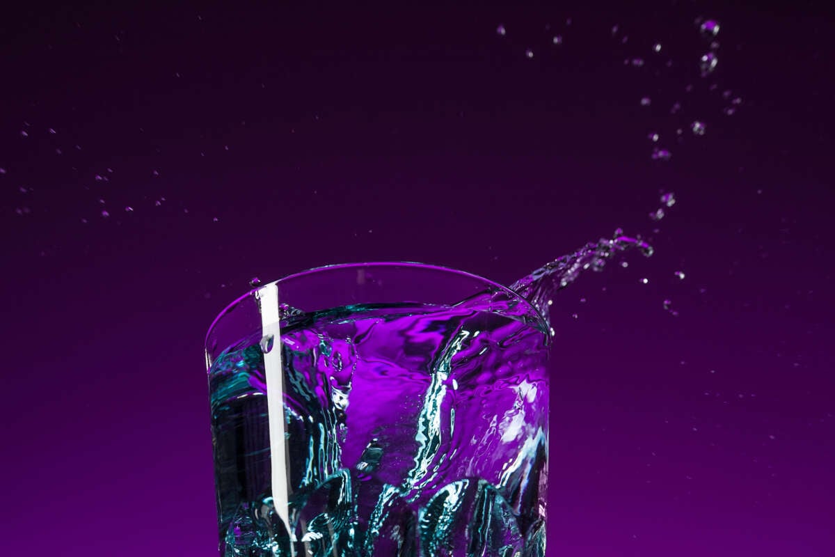 A glass of water splashes in front of purple-lit backdrop