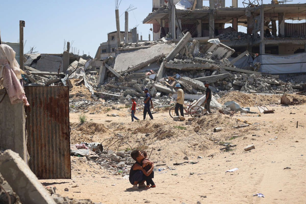 A Palestinian child hugs a toddler surrounded by destroyed buildings in Khan Yunis, in the southern Gaza Strip, on June 11, 2024.