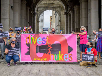 People stand behind a banner reading "Divest New York Nukes" during an outdoor demonstration