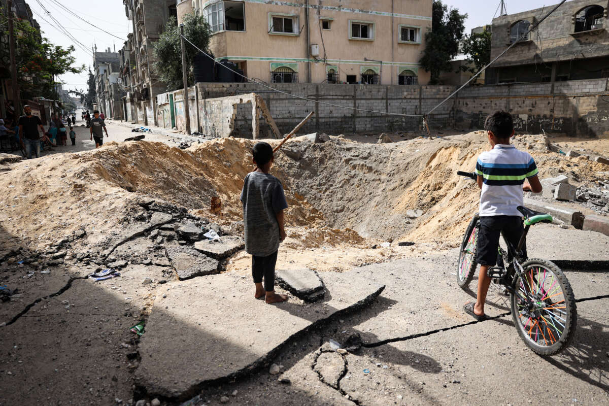 Children stand near a crater caused by Israeli bombardment in a street in Rafah in the southern Gaza Strip on May 18, 2024.