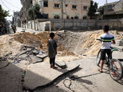 Children stand near a crater caused by Israeli bombardment in a street in Rafah in the southern Gaza Strip on May 18, 2024.