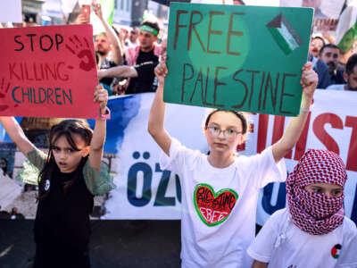 Two kids hold signs reading "STOP KILLING CHILDREN" and "FREE PALESTINE" during an outdoor protest