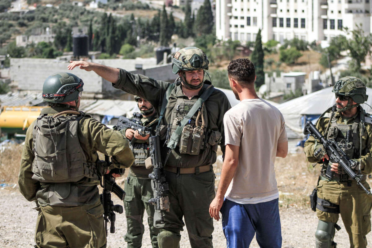 Israeli soldiers argue with a Palestinian man after an attack by settlers in the village of Burin, south of Nablus, in which Palestinian vehicles were burned and destroyed, on June 18, 2024.