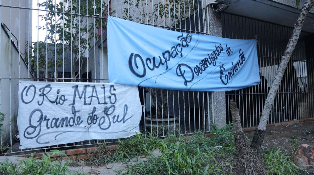 Two homemade banners are tied up to the metal fence out front in front of the occupation. The longer one reads, in Portuguese, Ocupação Desabrigados da Enchente — The Homeless from the Flood Occupation.