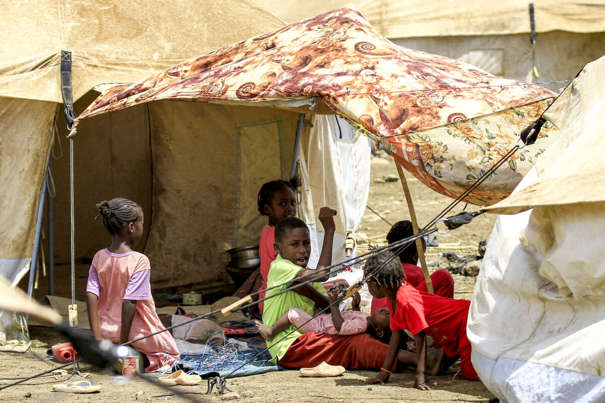 Children sit in the shade of a sheet outside a tent at a camp for people displaced by conflict in Sudan's eastern Gedaref province, on May 15, 2024.