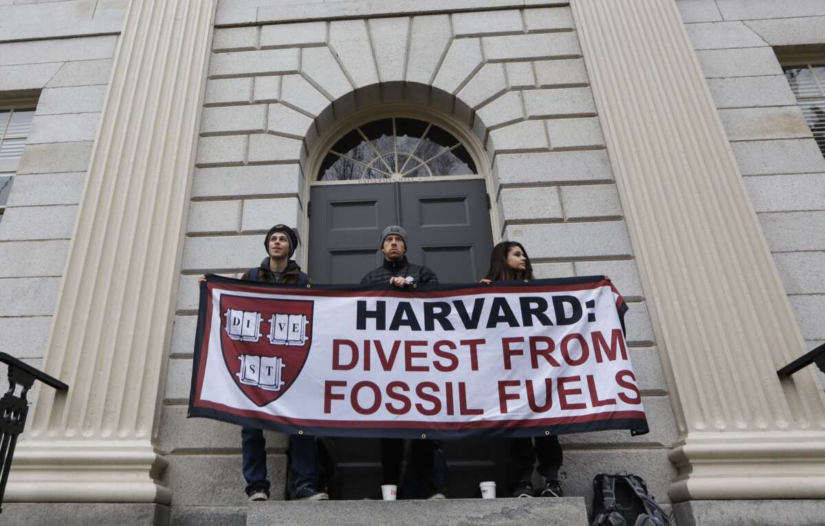 Students hold sign saying "Harvard: Divest from fossil fuels"