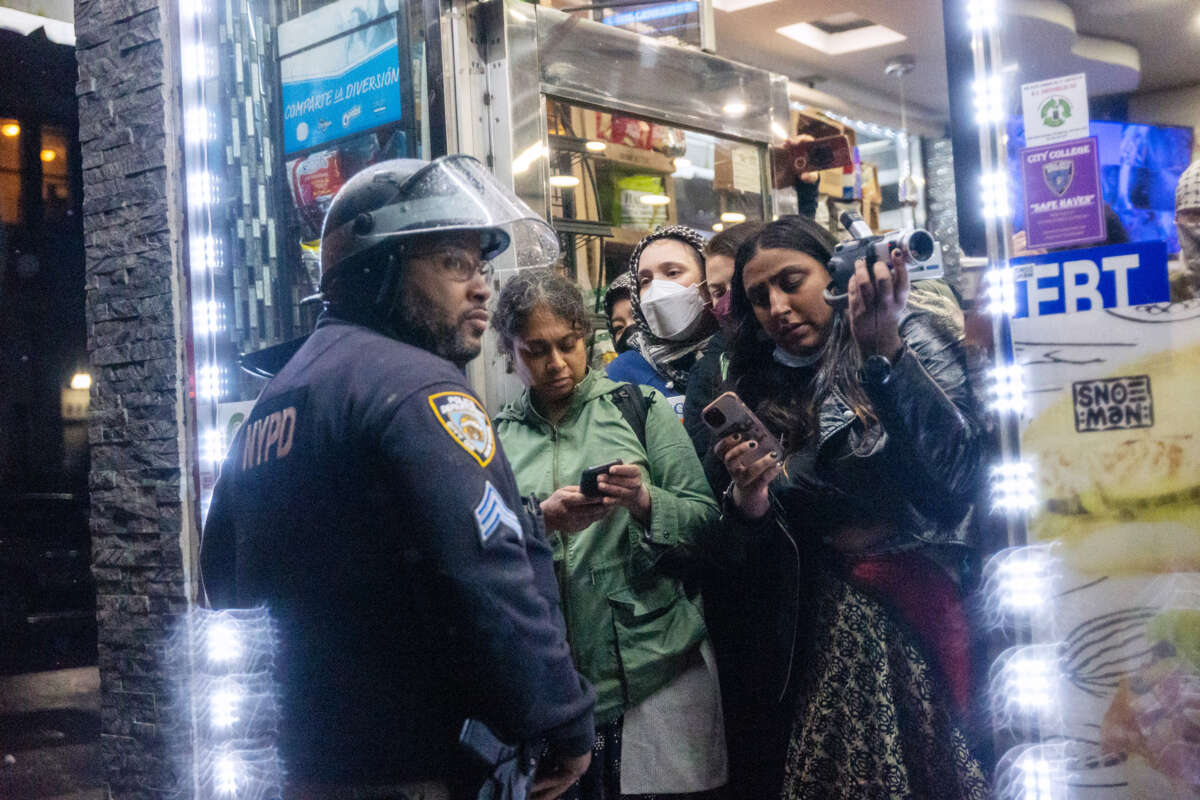 People inside of a shop try to take videos of a nearby protest as a cop stands in their way