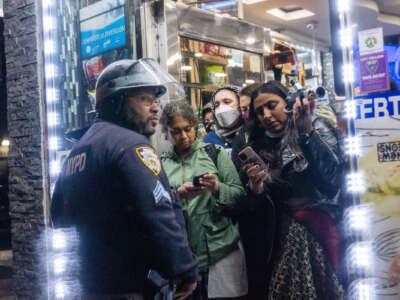 People inside of a shop try to take videos of a nearby protest as a cop stands in their way
