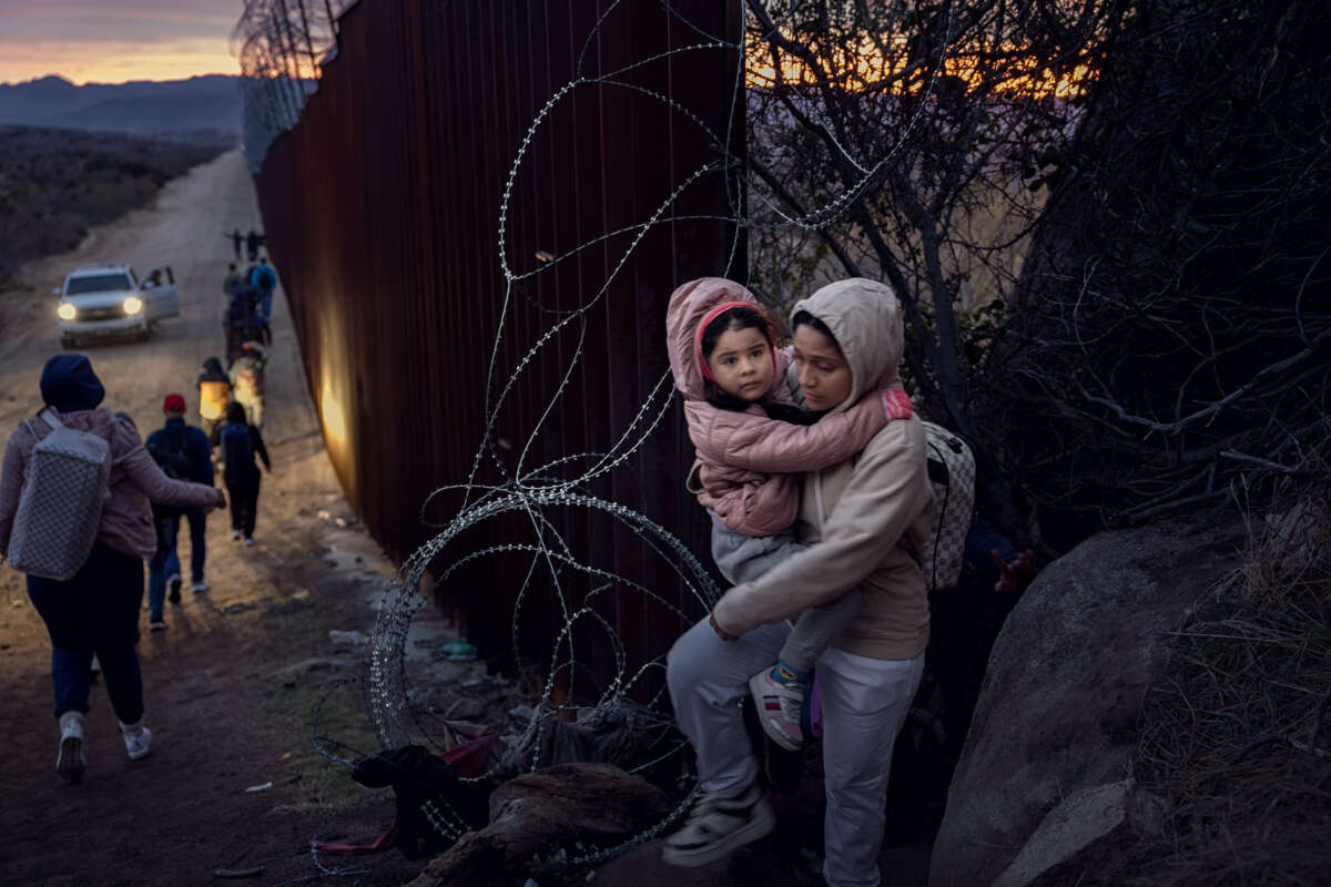 A woman carries her baby as they cross through a hole in a fence