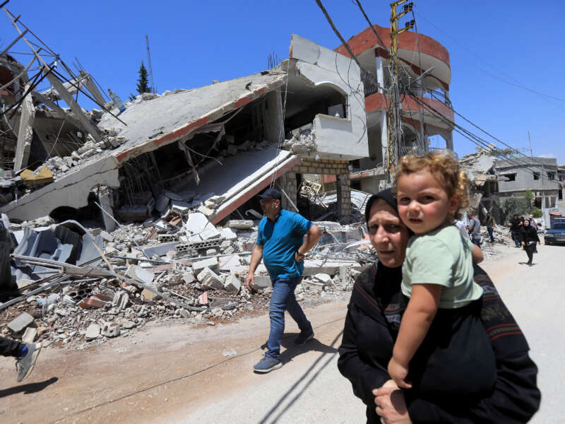 A woman carries a child as she walks past buildings destroyed during previous Israeli military fire on the southern Lebanese village of Aita al-Shaab, near the border with northern Israel, on June 29, 2024.