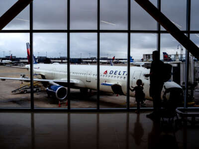 Passengers stand at the windows of an airport gate to look at the Delta airplane parked outside