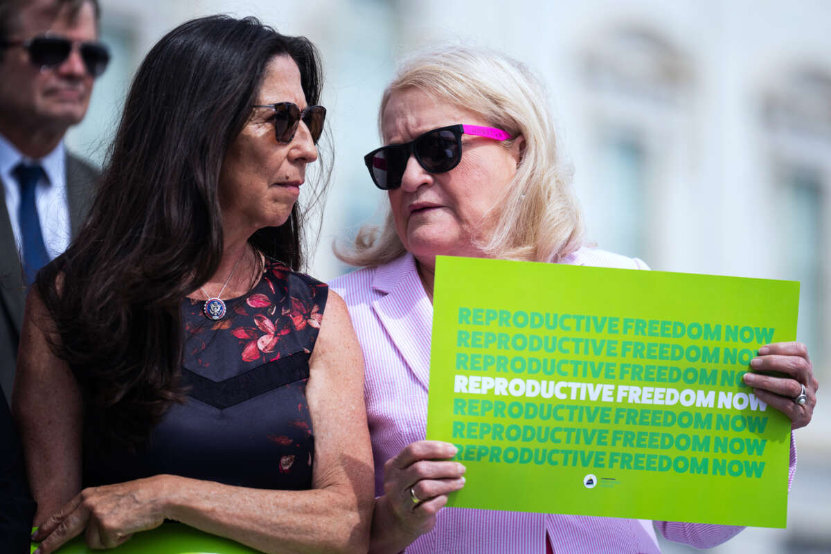 Rep Sylvia Garcia holds a sign reading "REPRODUCTIVE FREEDOM NOW" while speaking quietly to Teresa Leger Fernandez, standing beside her