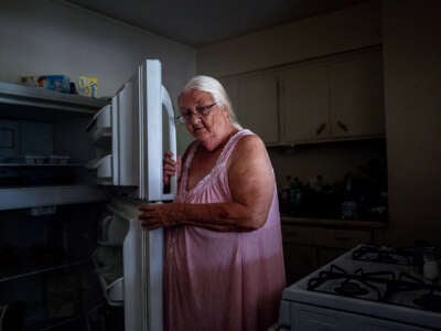 An elderly woman opens her dark and empty refrigerator