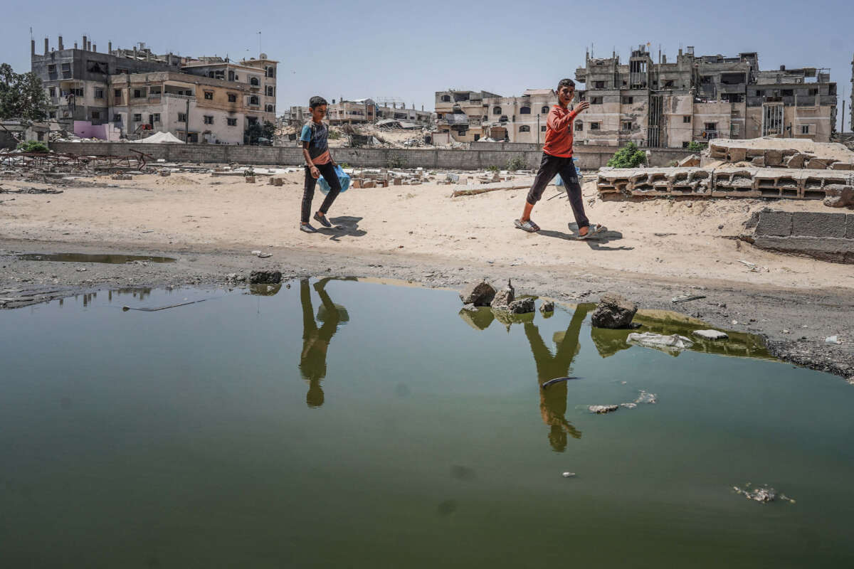 Two Palestinian boys walk past stagnant pools of water in Khan Yunis in the southern Gaza Strip on July 19, 2024.