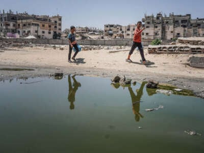 Two Palestinian boys walk past stagnant pools of water in Khan Yunis in the southern Gaza Strip on July 19, 2024.