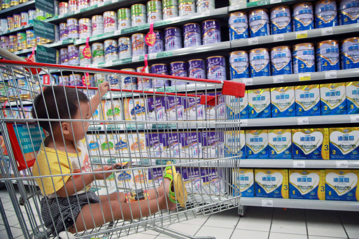 A baby sits in a shopping cart in the formula aisle of a grocery store