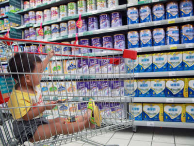 A baby sits in a shopping cart in the formula aisle of a grocery store