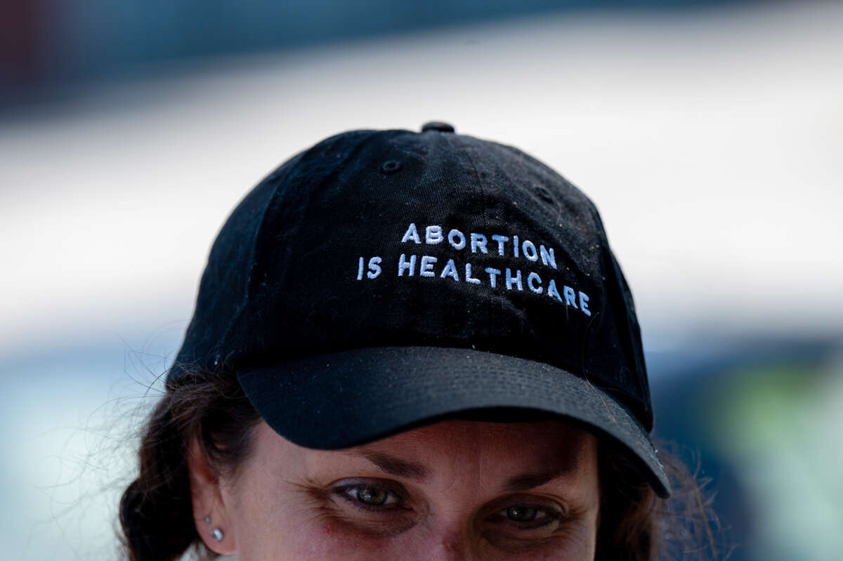 A woman wears a black hat with white text reading "ABORTION IS HEALTHCARE"