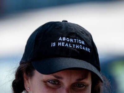 A woman wears a black hat with white text reading "ABORTION IS HEALTHCARE"