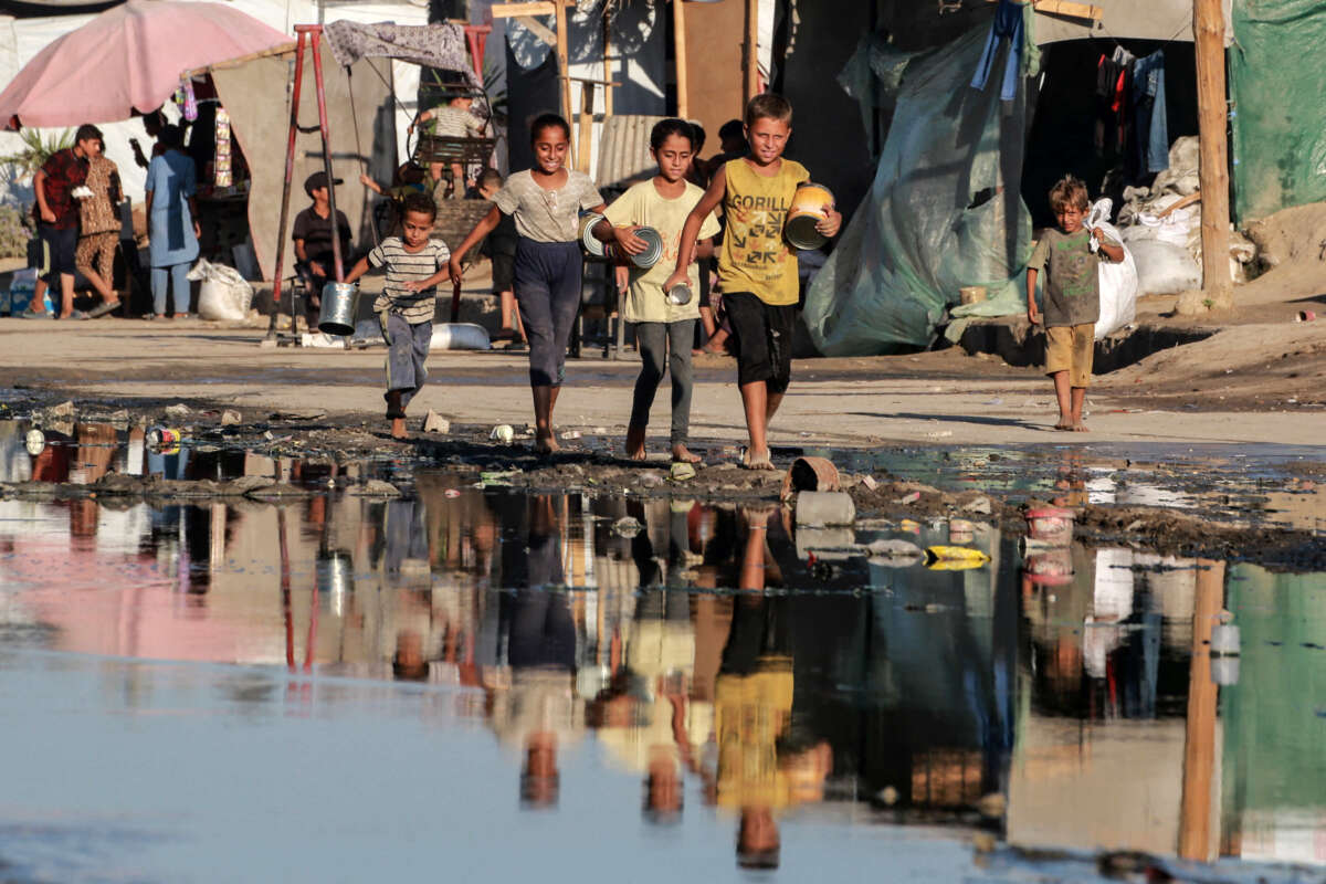 Palestinian children carrying empty containers walk near stagnant wastewater, on their way to a food distribution point in Deir el-Balah in the central Gaza Strip on July 19, 2024.