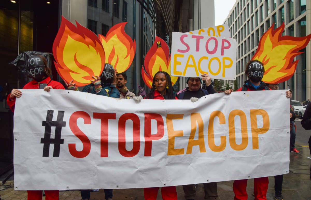 Protesters wearing 'Stop EACOP' masks hold a 'Stop EACOP' banner and cardboard cutouts resembling fire during the demonstration in London, U.K., on October 18, 2023.