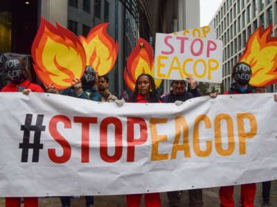 Protesters wearing 'Stop EACOP' masks hold a 'Stop EACOP' banner and cardboard cutouts resembling fire during the demonstration in London, U.K., on October 18, 2023.