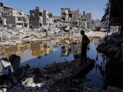 A Palestinian stands on the rubble of destroyed buildings as he looks at the a pool of stagnant water in Khan Yunis in the southern Gaza Strip on July 19, 2024.