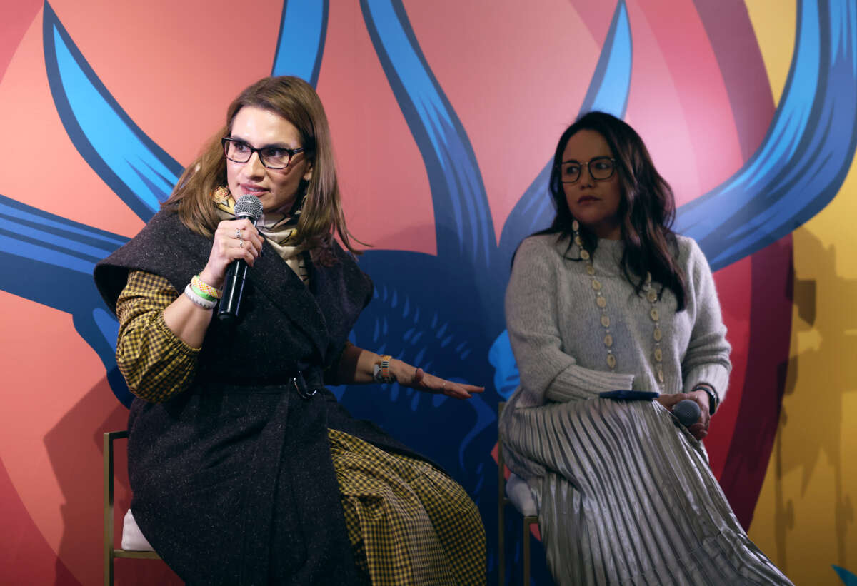 Lt. Governor Peggy Flanagan speaks into a handheld microphone while sitting beside Holly Cook Macarro