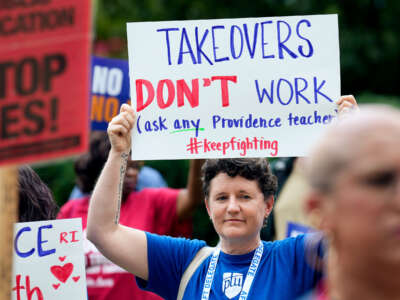 A teacher holds up a sign reading "TAKEOVERS DON'T WORK; (ask any Providence teacher)" during an outdoor protest