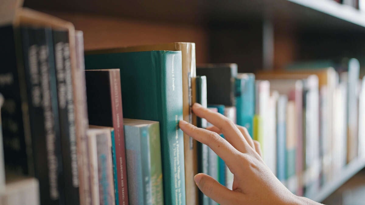 Close up hand search for book on bookshelves in the library.