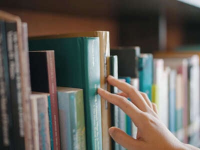 Close up hand search for book on bookshelves in the library.