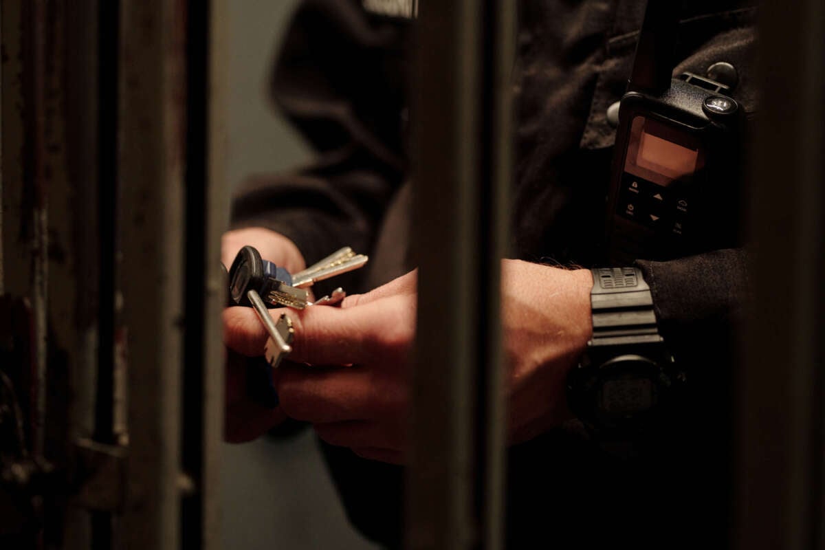 Hands of unrecognizable male prison guard in black uniform standing by gate looking at keys