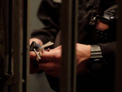 Hands of unrecognizable male prison guard in black uniform standing by gate looking at keys