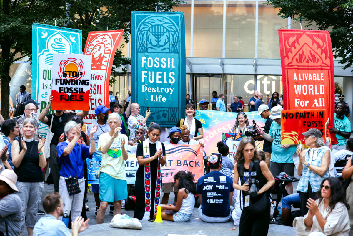 People with banners reading "FOSSIL FUELS DESTROY LIFE" and "A LIVEABLE WORLD FOR ALL" congregate in front of a citibank in protest of their investment in fossil fuels