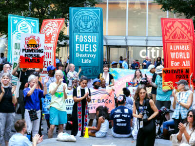 People with banners reading "FOSSIL FUELS DESTROY LIFE" and "A LIVEABLE WORLD FOR ALL" congregate in front of a citibank in protest of their investment in fossil fuels