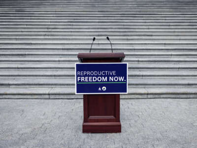 A sign on an empty podium on white granite steps reads "REPRODUCTIVE FREEDOM NOW"