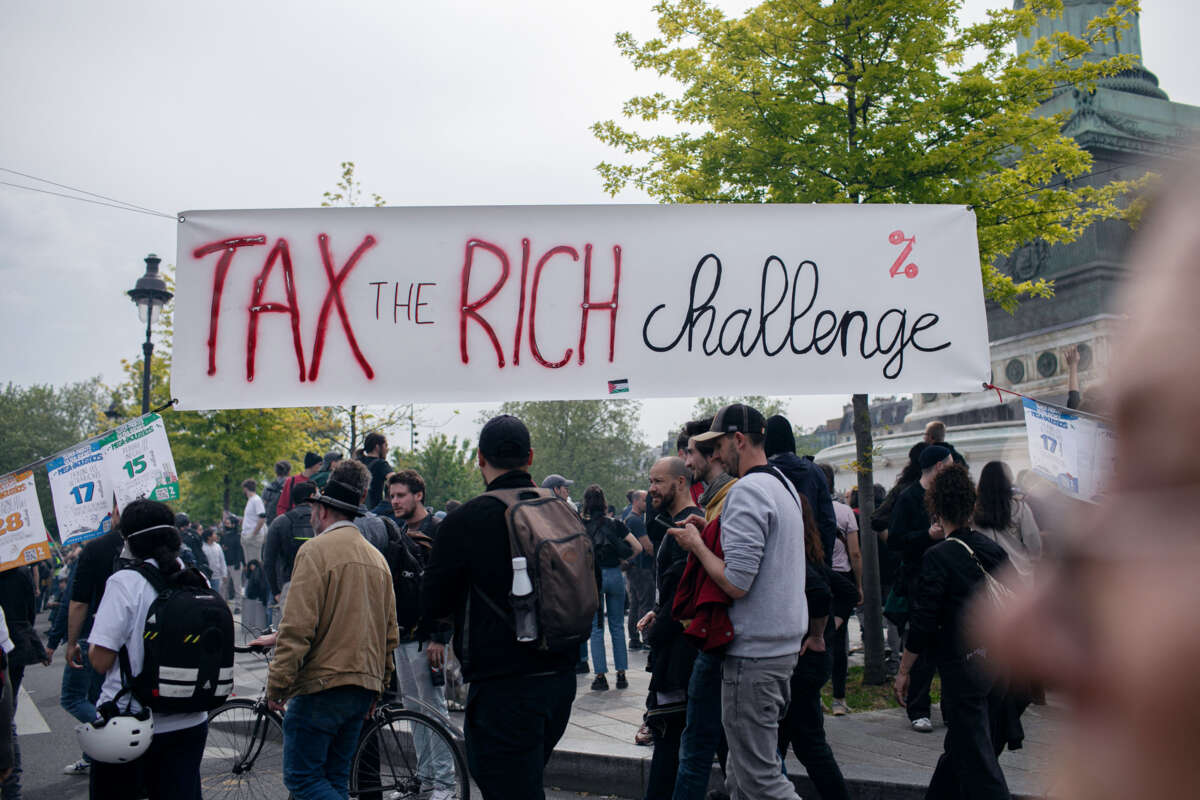 People walk under a banner reading "TAX THE RICH CHALLENGE"