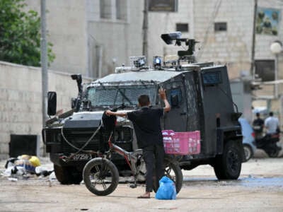 A Palestinian boy raises his arm into the air as Israeli soldiers inspect what he is carrying during a raid in Jenin in the occupied West Bank on August 28, 2024.