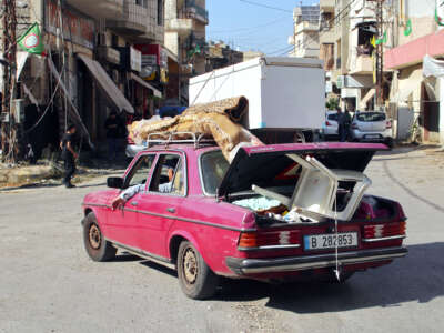 A family in a maroon car drive with their belongings tied to its roof