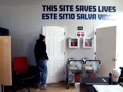 A person exits a room with the text "THIS SITE SAVES LIVES" painted on the wall in both English and Spanish