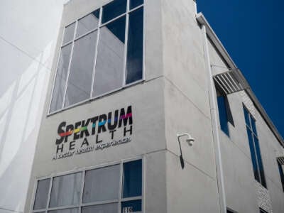 An exterior shot of Spektrum health, showing its logo, along with its tagline "A better health experience", on a concrete wall between two windows