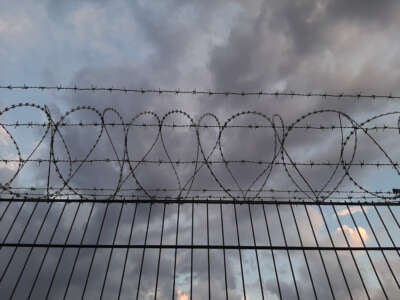 Low angle view of barbed wire atop fence with cloudy sky.