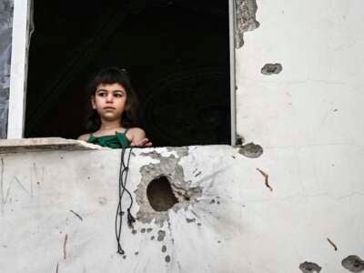 A Palestinian girl looks out of the window of a shrapnel-pocked building in Jenin in the aftermath of a raid by Israeli forces in the occupied West Bank city on May 23, 2024.