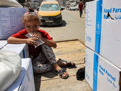 A girl holds a clear plastic bag filled with water as she sits atop a cart next to humanitarian aid packages provided by the United Nations Relief and Works Agency for Palestine Refugees (UNRWA) in central Gaza City on August 27, 2024.