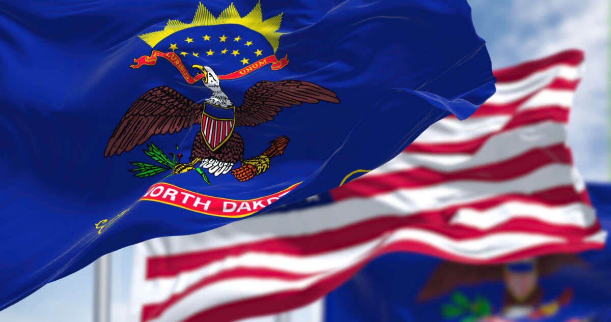 North Dakota state flags and USA flag fly against cloudy sky