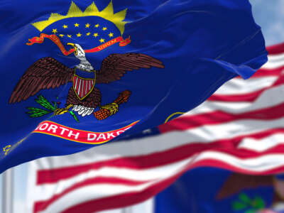 North Dakota state flags and USA flag fly against cloudy sky