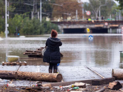 a woman stands in a flooded street and looks toward a bridge